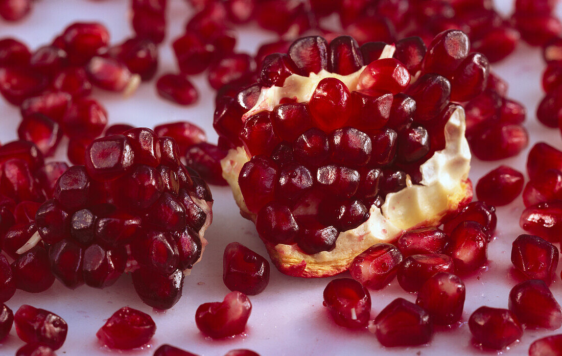 One piece of pomegranate surrounded by many pomegranate seeds