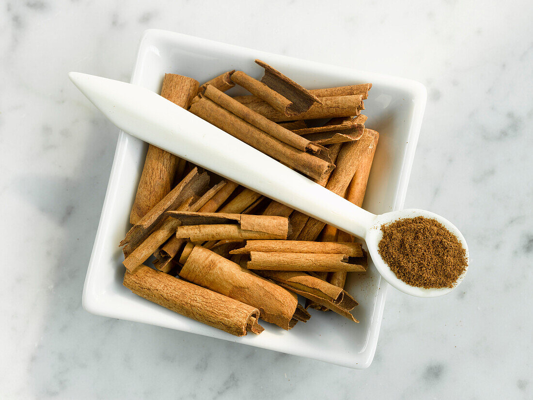 Bowl with cinnamon sticks and spoon with ground cinnamon