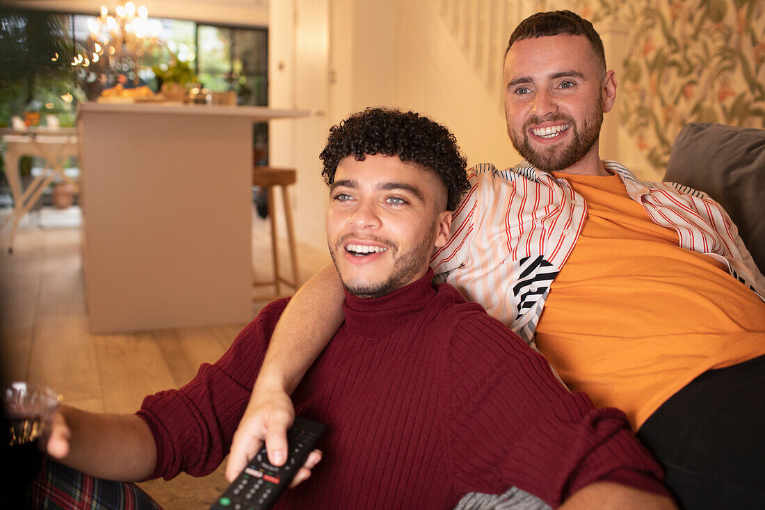 Happy gay male couple watching TV on sofa