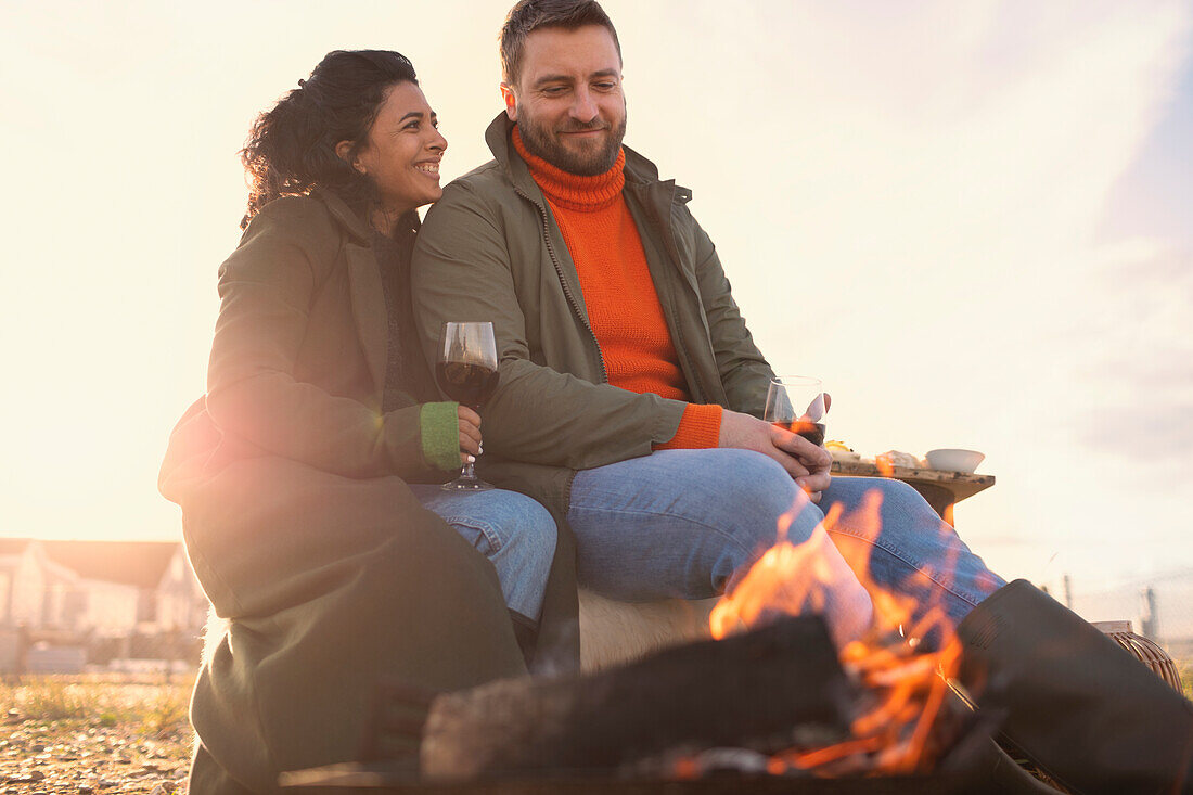 Happy couple enjoying red wine by fire on winter beach