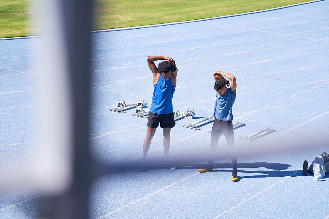 Male runners stretching on sunny blue sports track