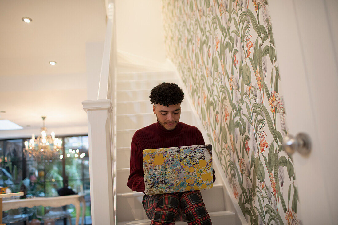 Young man using laptop on apartment stairs