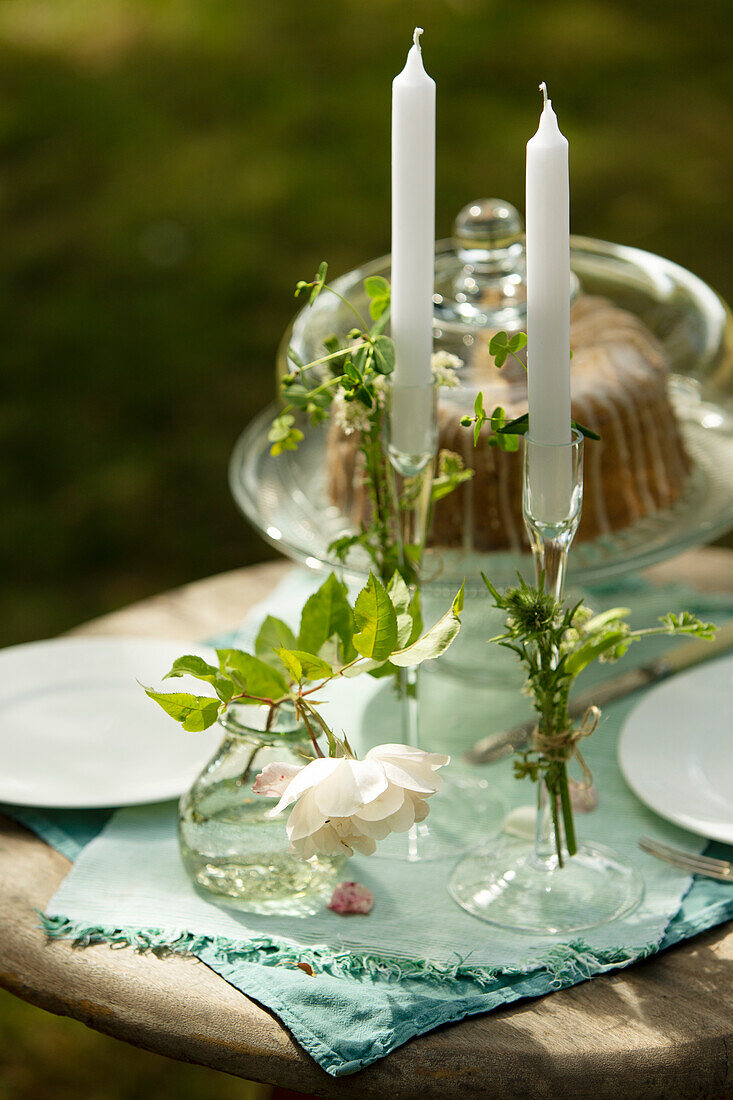 Candlesticks and rose on garden table with cake