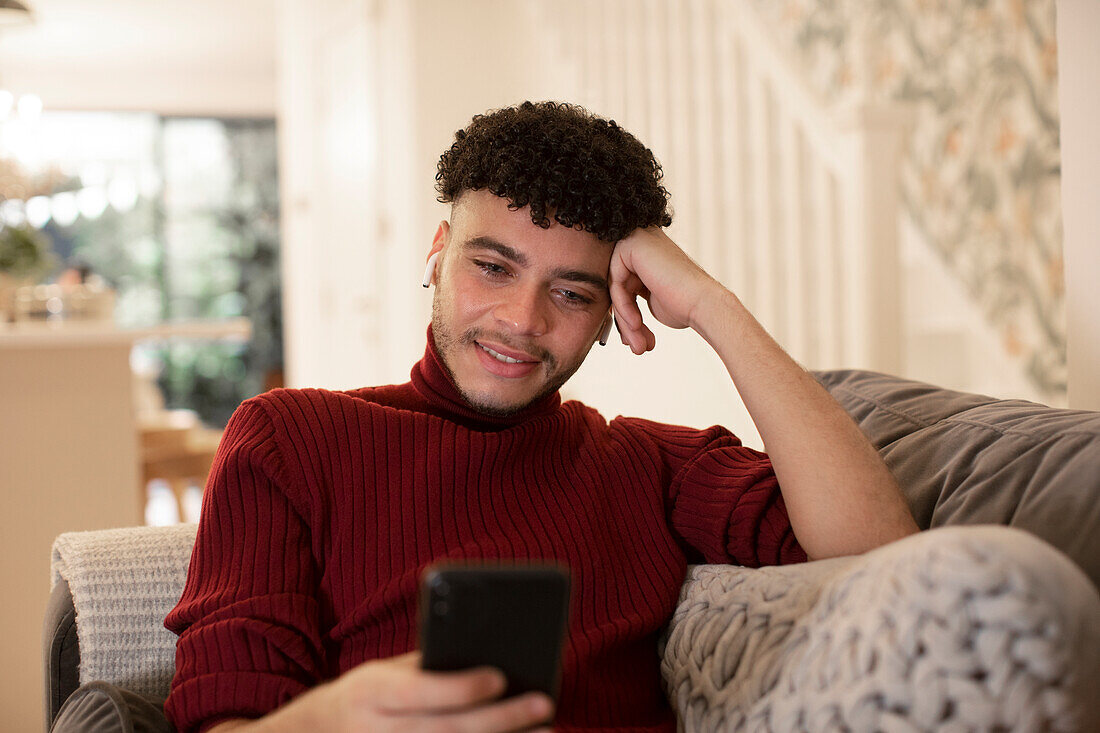 Young man using smart phone on living room sofa