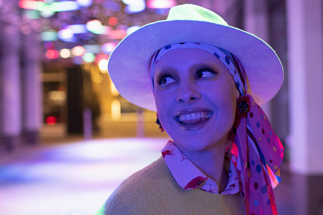 Happy woman in headscarf and fedora under neon light