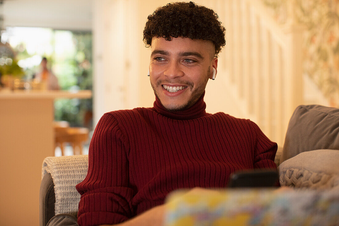 Happy young man listening to music with earbuds on sofa