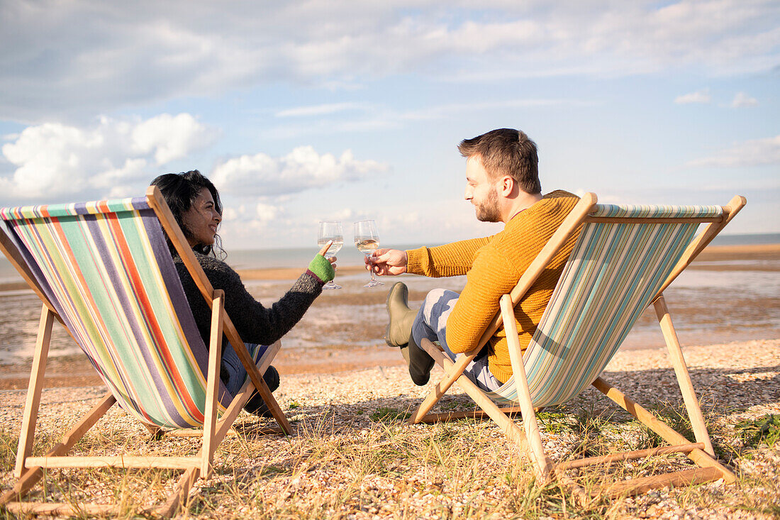 Happy couple toasting wine glasses on sunny winter beach