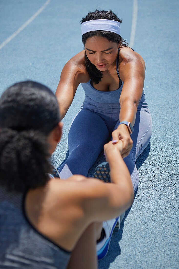 Female track and field athletes stretching on sunny track