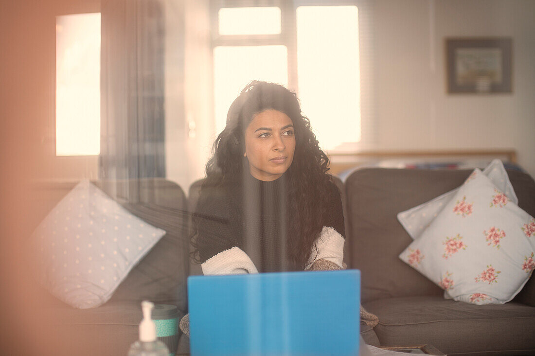 Woman with headphones working from home on laptop on sofa