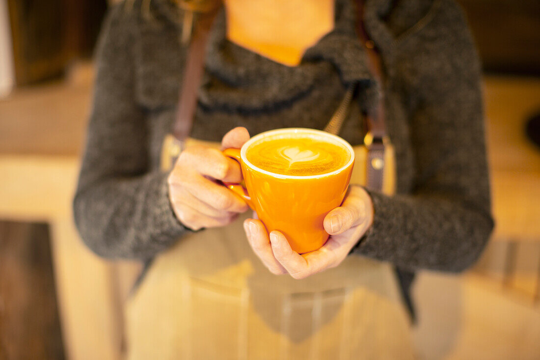 Female barista holding cappuccino with heart foam
