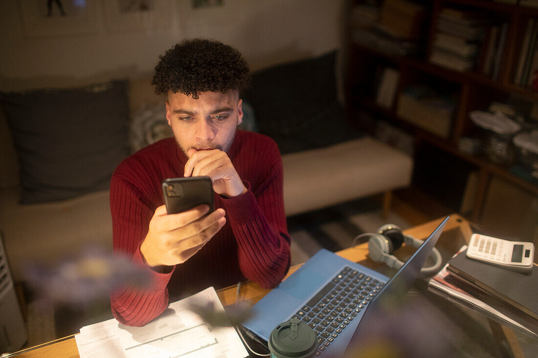 Young man with smart phone working from home on laptop