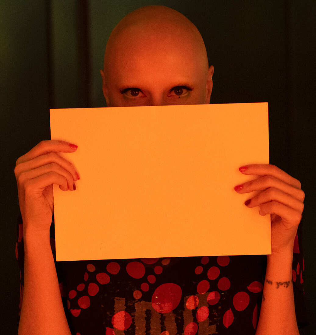 Woman with shaved head holding blank paper