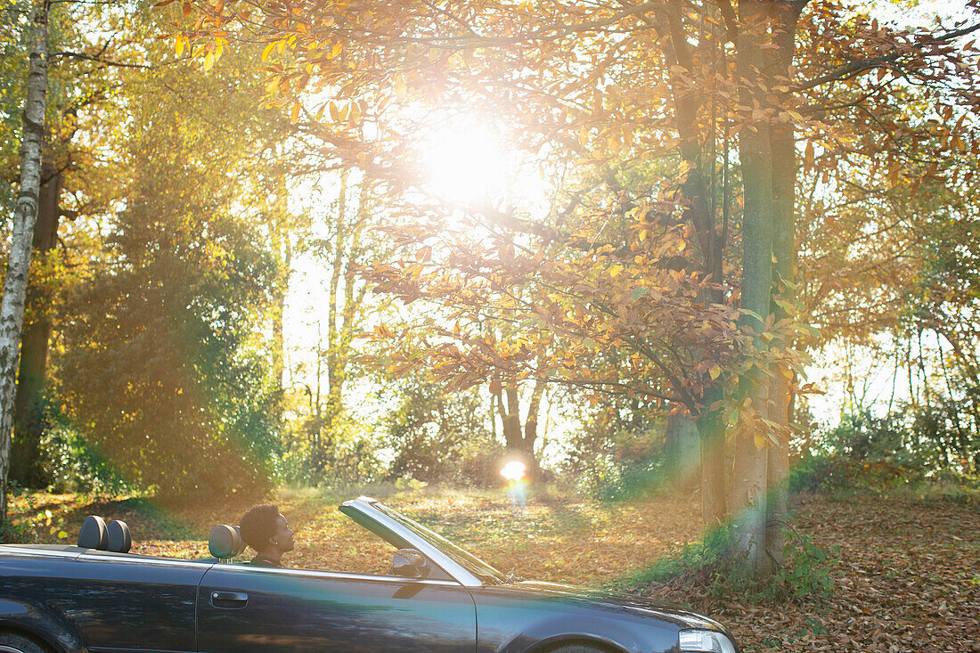 Woman driving convertible in sunny autumn park