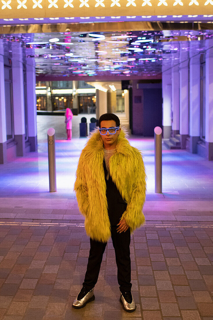 Young man in feather coat under neon city lights