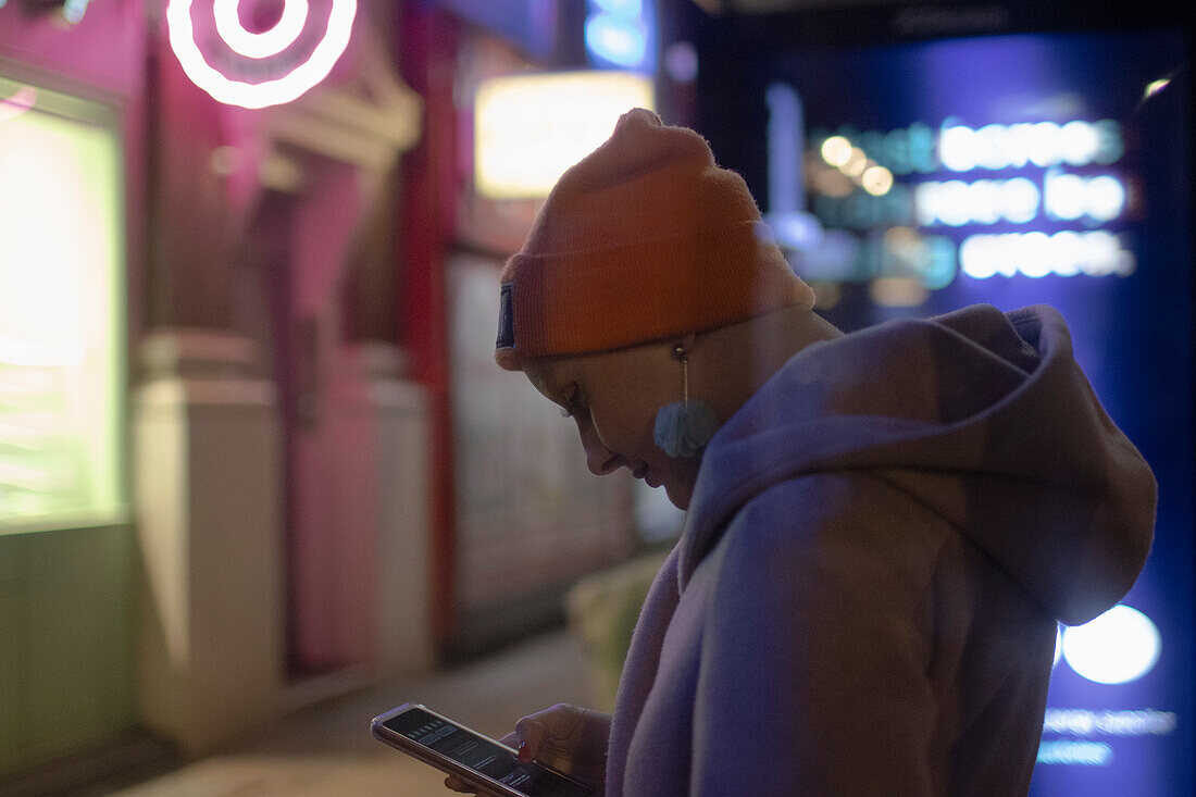 Woman using smart phone on city sidewalk at night