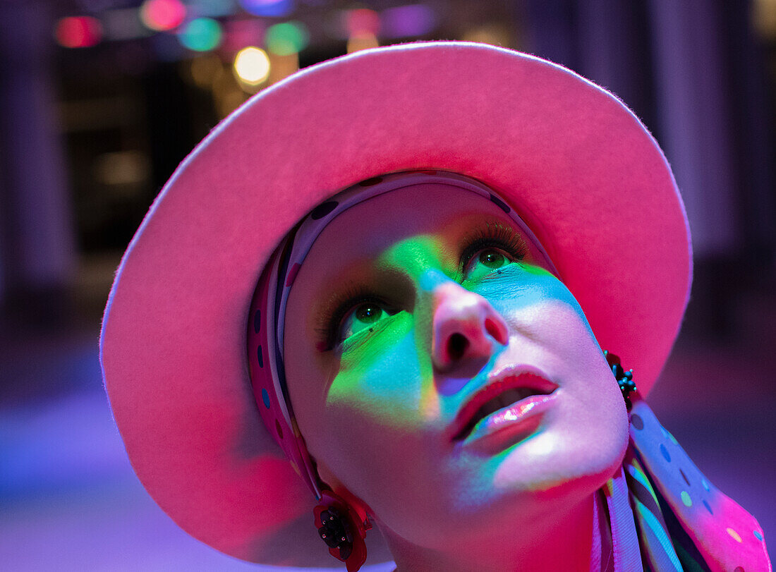 Curious woman in pink hat looking up in neon light