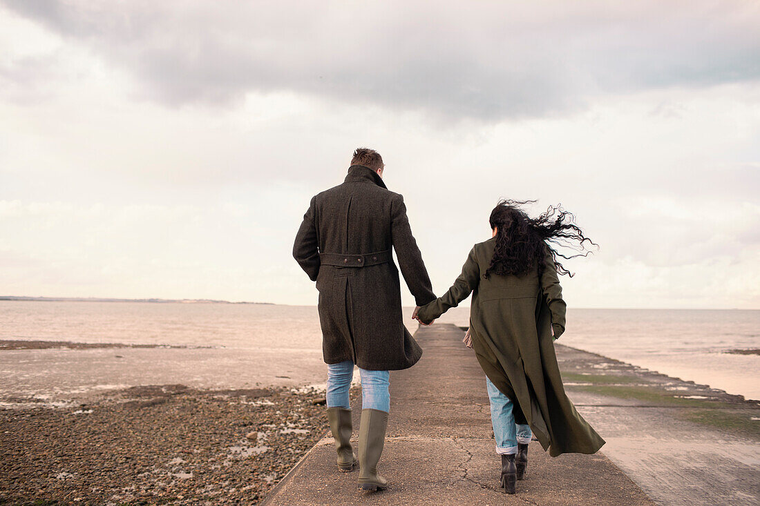 Couple in winter coats holding hands on beach jetty