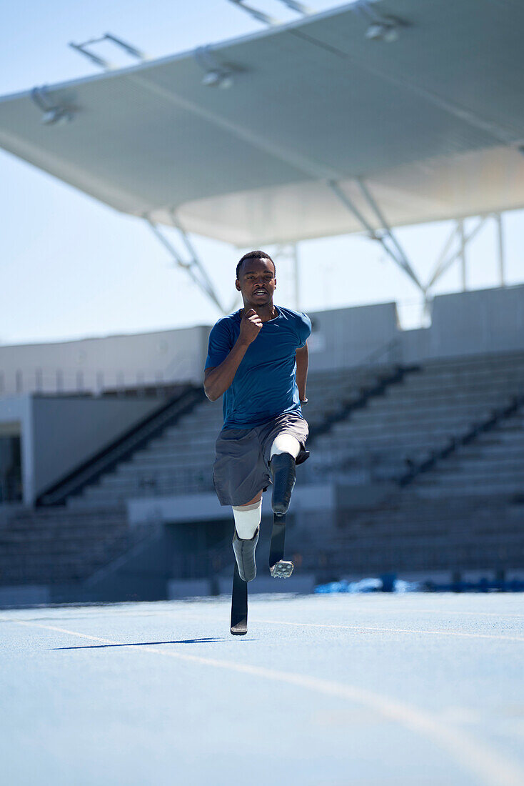 Young amputee athlete running on sunny blue sports track