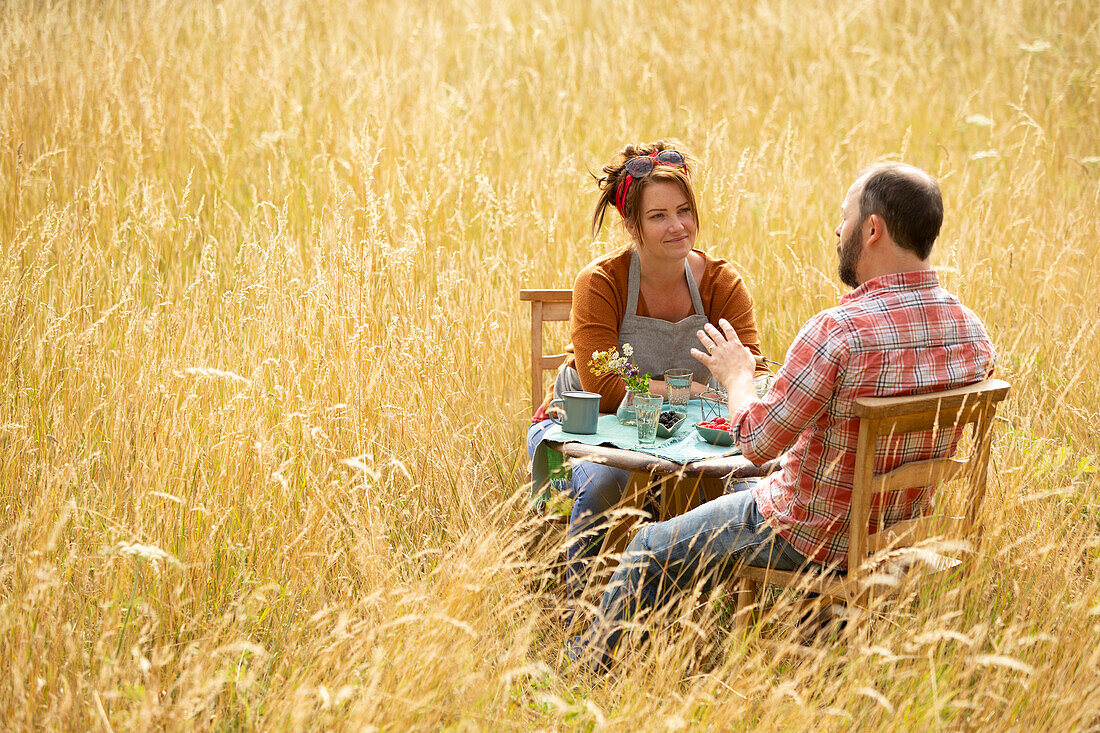 Couple talking and eating berries at table in tall grass