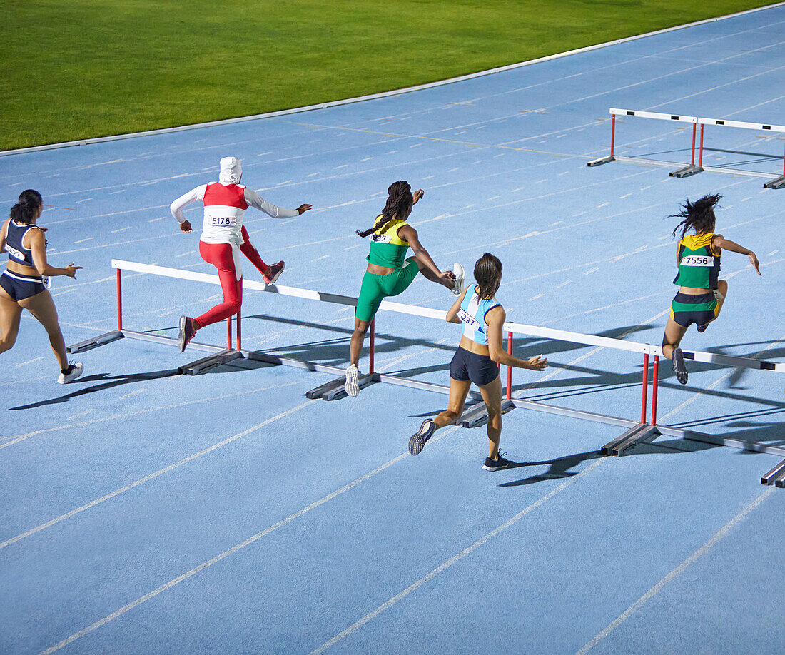 Female athletes jumping hurdles in competition