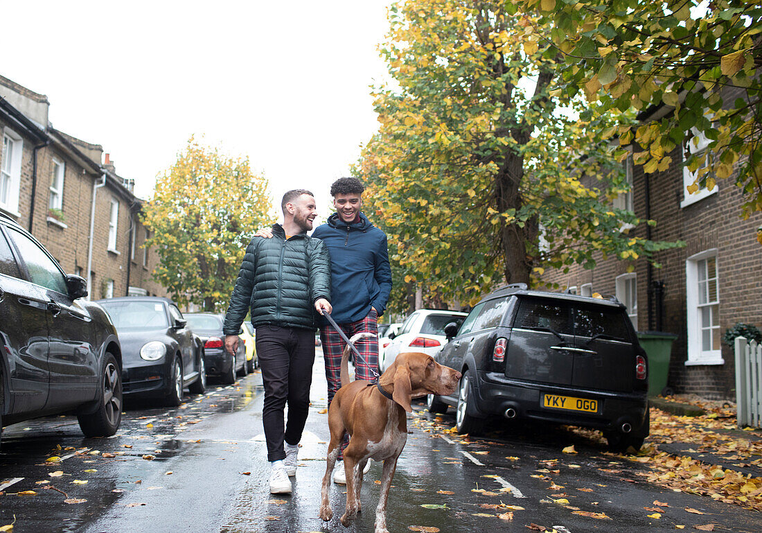 Gay couple walking dog on leash on wet autumn city street