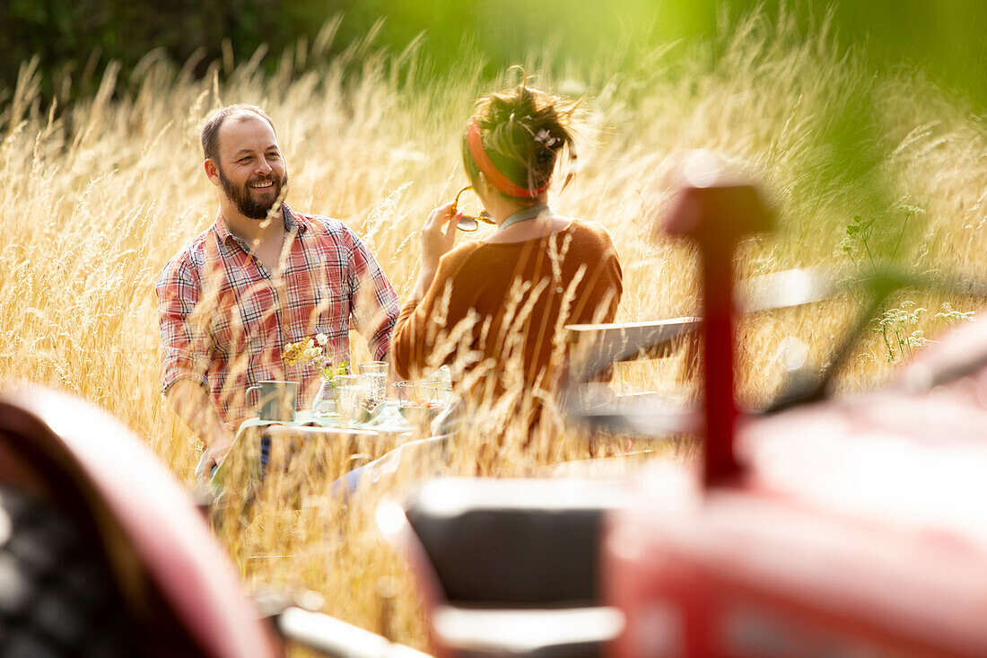 Happy couple at table behind tractor in summer tall grass
