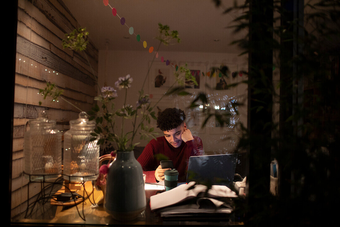 Young man with smart phone working from home at night