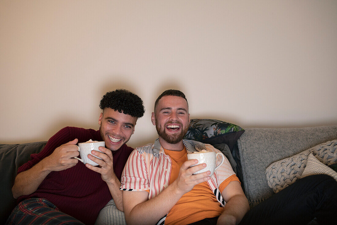 Happy gay couple drinking hot cocoa and watching TV on sofa