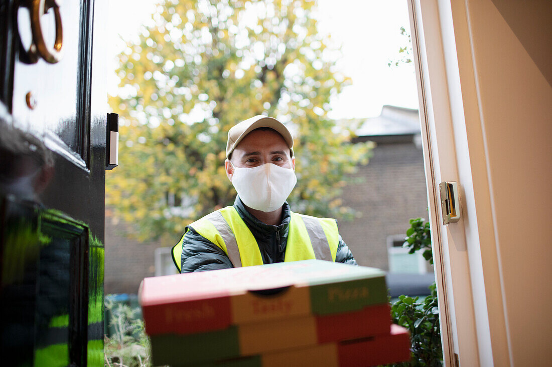 Delivery man in face mask delivering pizza at front door