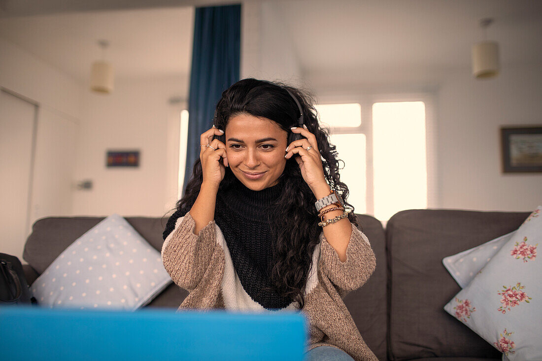 Smiling woman with headphones working from home on sofa