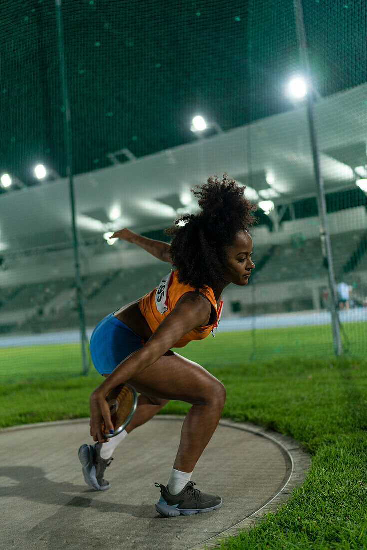 Female athlete throwing discus in stadium at night