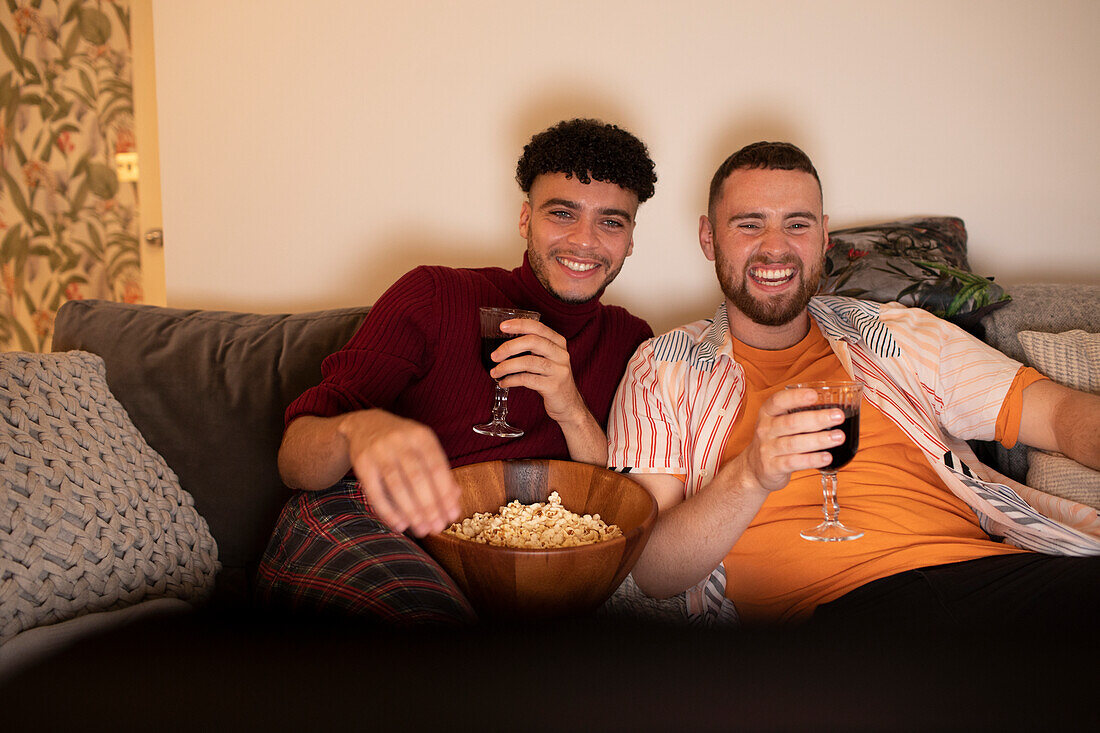 Happy gay couple with wine and popcorn watching movie