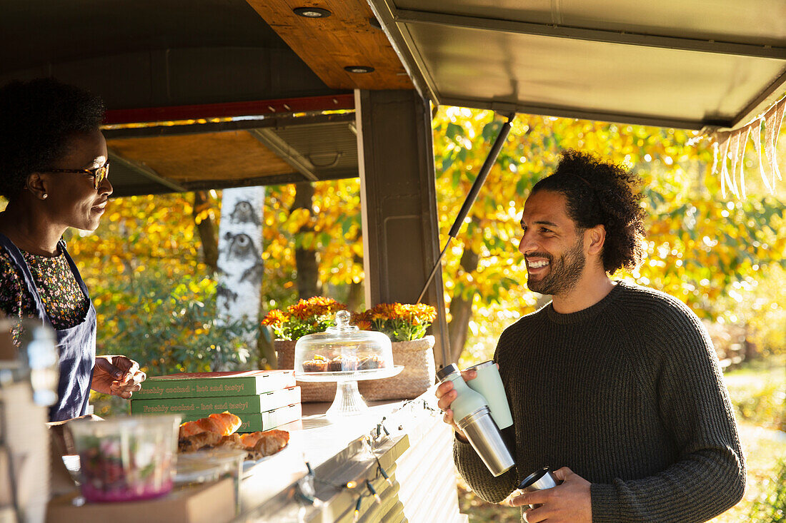 Happy customer talking with food cart owner in autumn park