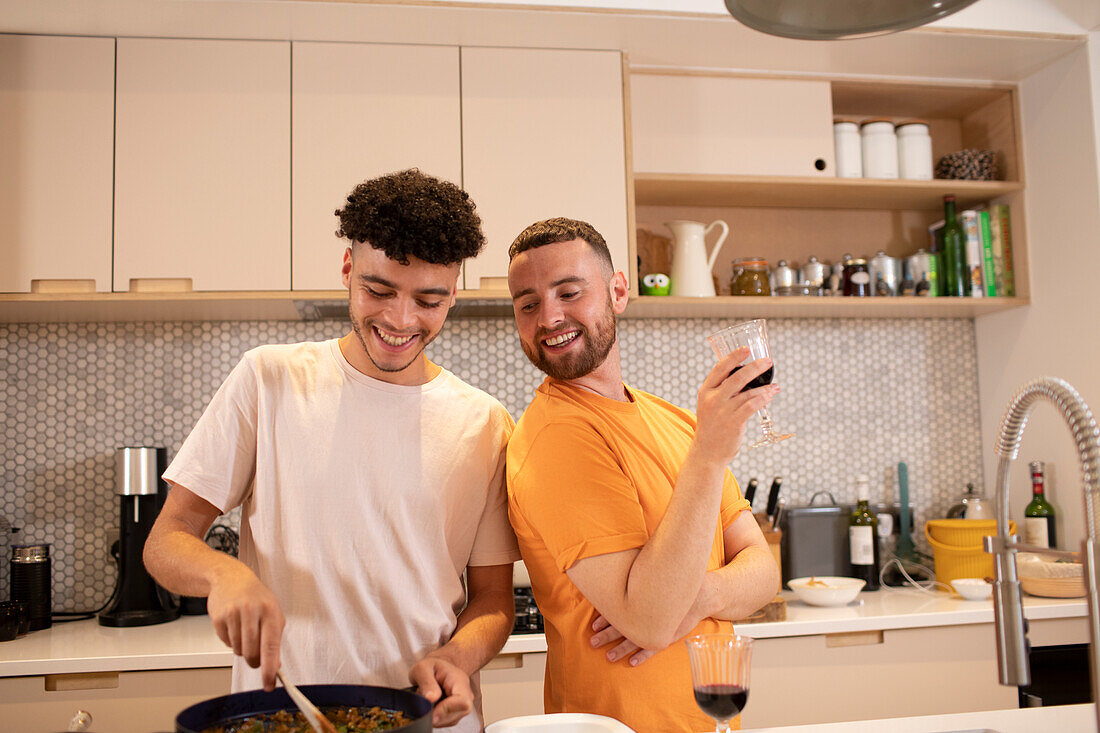 Happy gay male couple cooking and drinking wine in kitchen