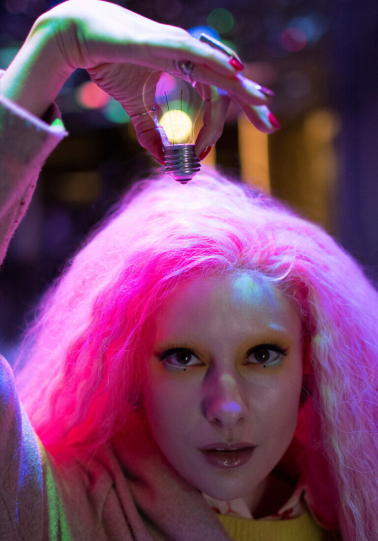 Woman with pink hair holding light bulb over head