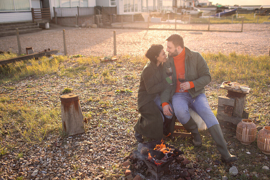 Couple in winter coats enjoying wine by fire on beach patio