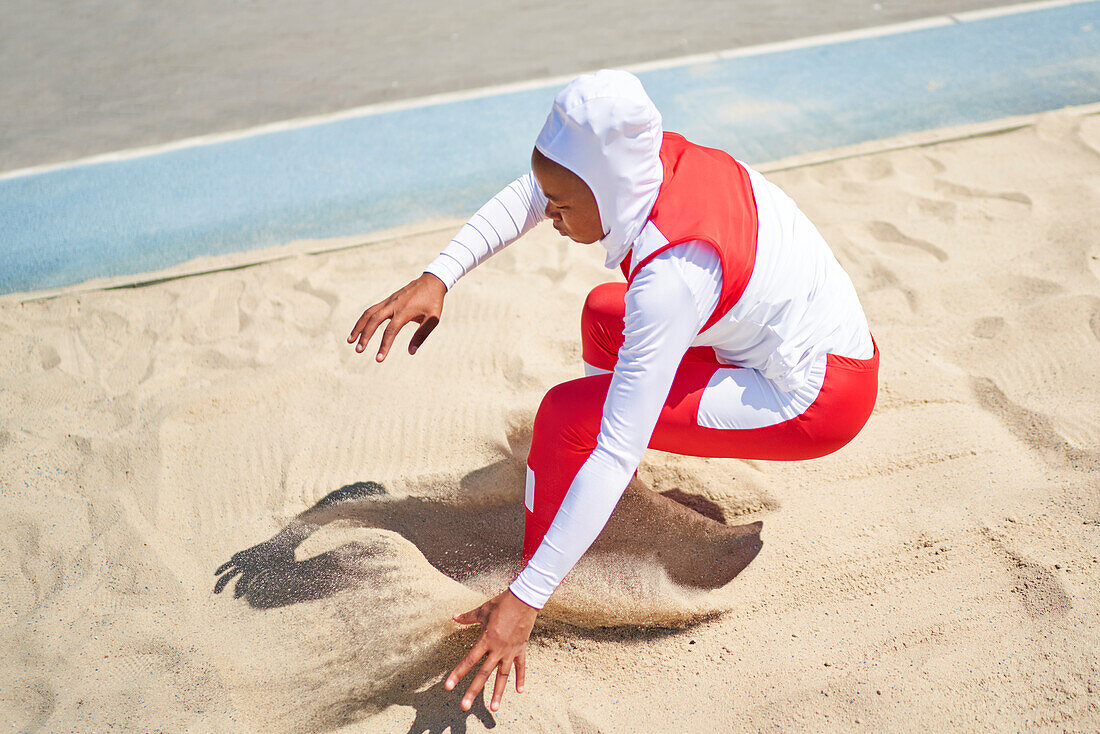 Female track and field athlete in hijab long jumping in sand