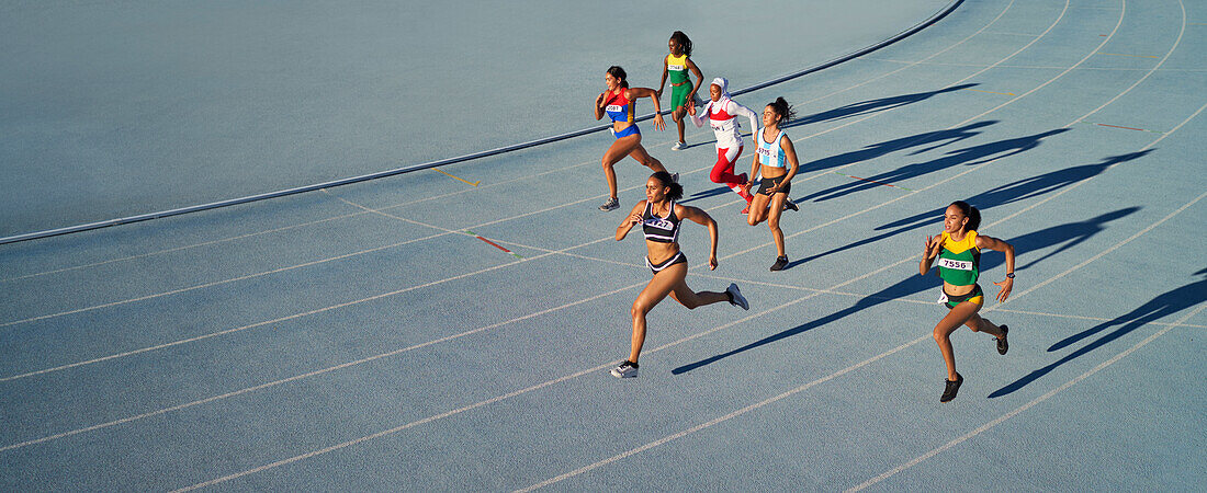 Female athletes running in race on blue track