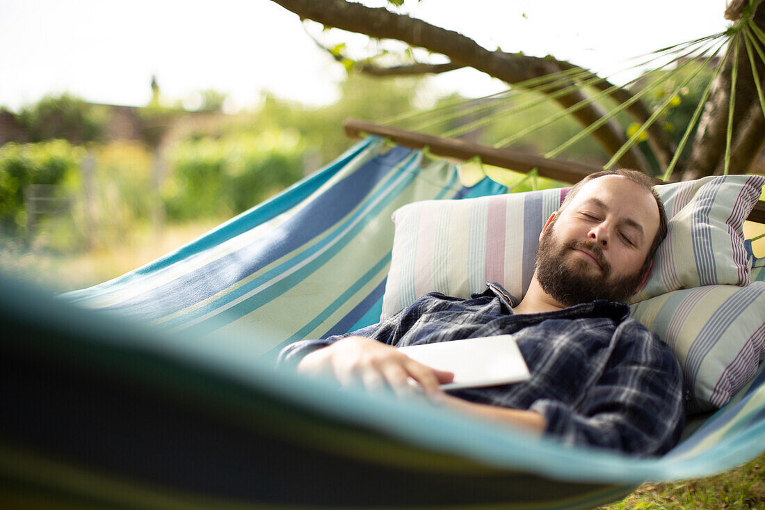 Man with digital tablet sleeping in backyard summer hammock