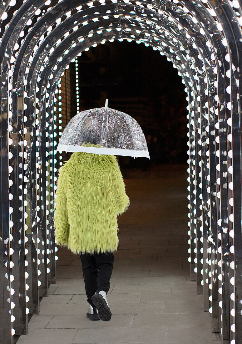 Man in feather coat with umbrella under arch lights