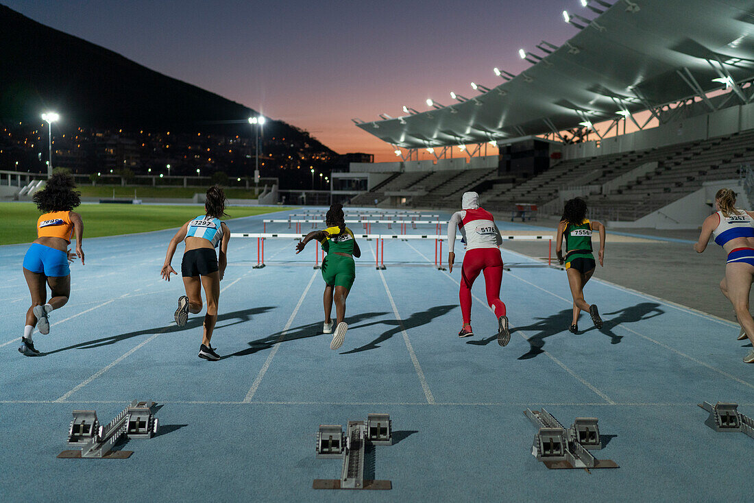 Female athletes racing to hurdles on track at night
