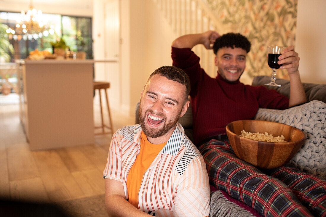 Happy gay couple with wine and popcorn watching TV