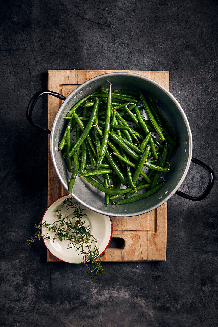 Fresh beans in an aluminium sieve and herbs on an enamel plate