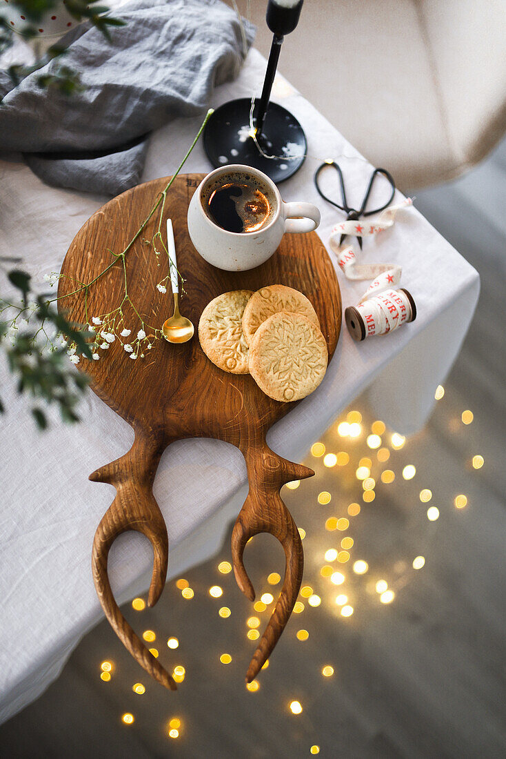 Christmas biscuits and a cup of coffee on a wooden board in the shape of antlers