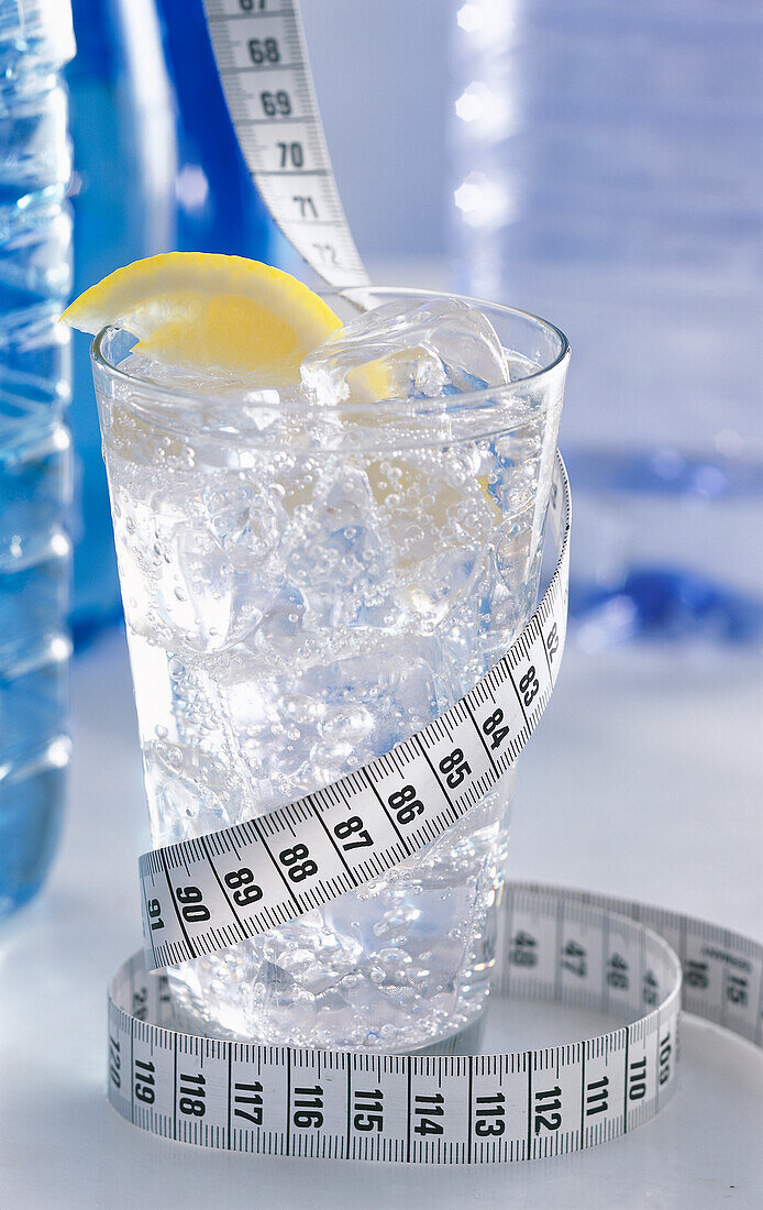 A glass of water with ice cubes and lemon wrapped in a measuring tape