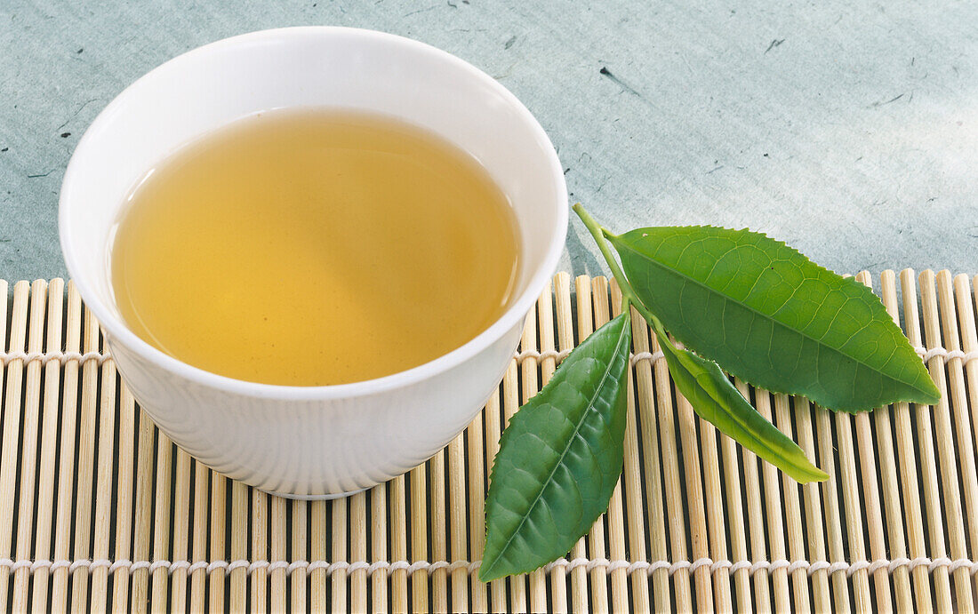 Grüner Tee in einer Trinkschale neben frischen Teeblättern