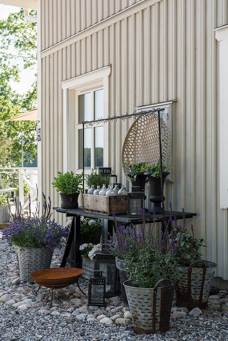 Gartentisch mit Urnenvasen und Flaschenträger und Lavendeltöpfe auf Kiesboden an Hauswand