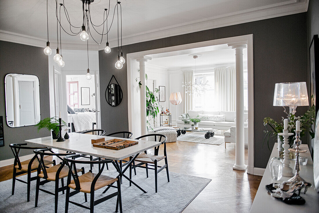 Classic chairs around dining table with marble top below pendant light in room with grey walls