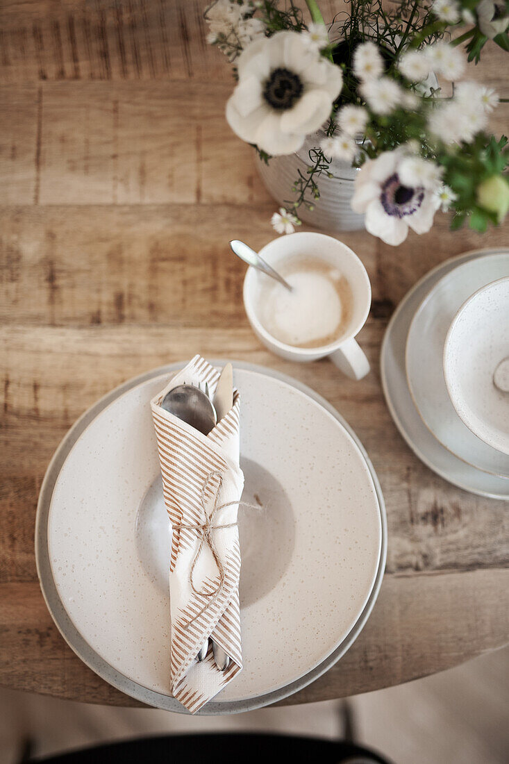 Gedeck in Naturfarben, Kaffeetasse und Blumenstrauß auf Holztisch