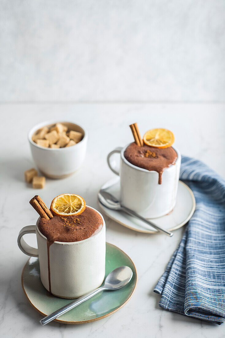 Two cups of hot chocolate decorated with cinnamon and orange